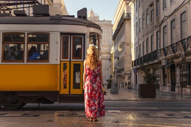 Jeune touriste blonde regardant passer le tramway jaune typique de Lisbonne dans la rue du centre ville sur la Rua Augusta.